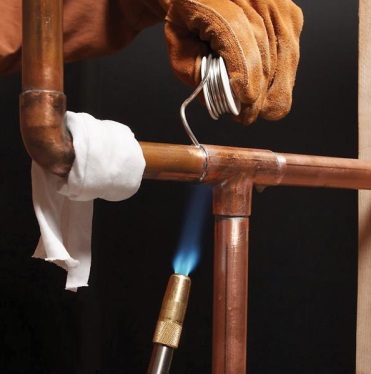 A copper tee being soldered with a blowtorch