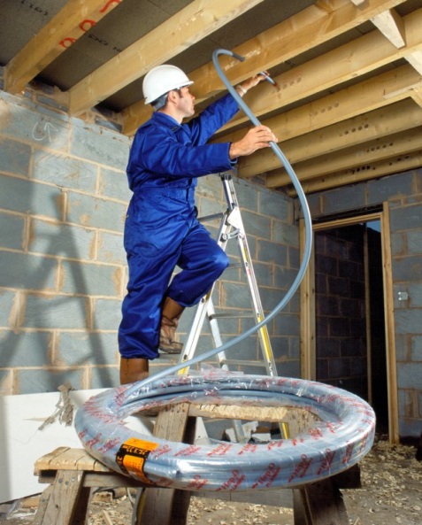 An operative pulling a coil of plastic pipe through a joisted floor