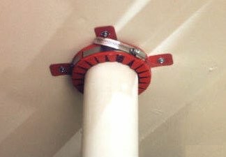 A red intumescent fire collar fitted around a plastic soil pipe where it passes through a fire-rated wall or floor