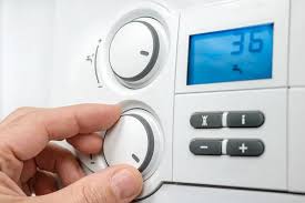 Hand adjusting the dial on a central heating boiler programmer with digital temperature display